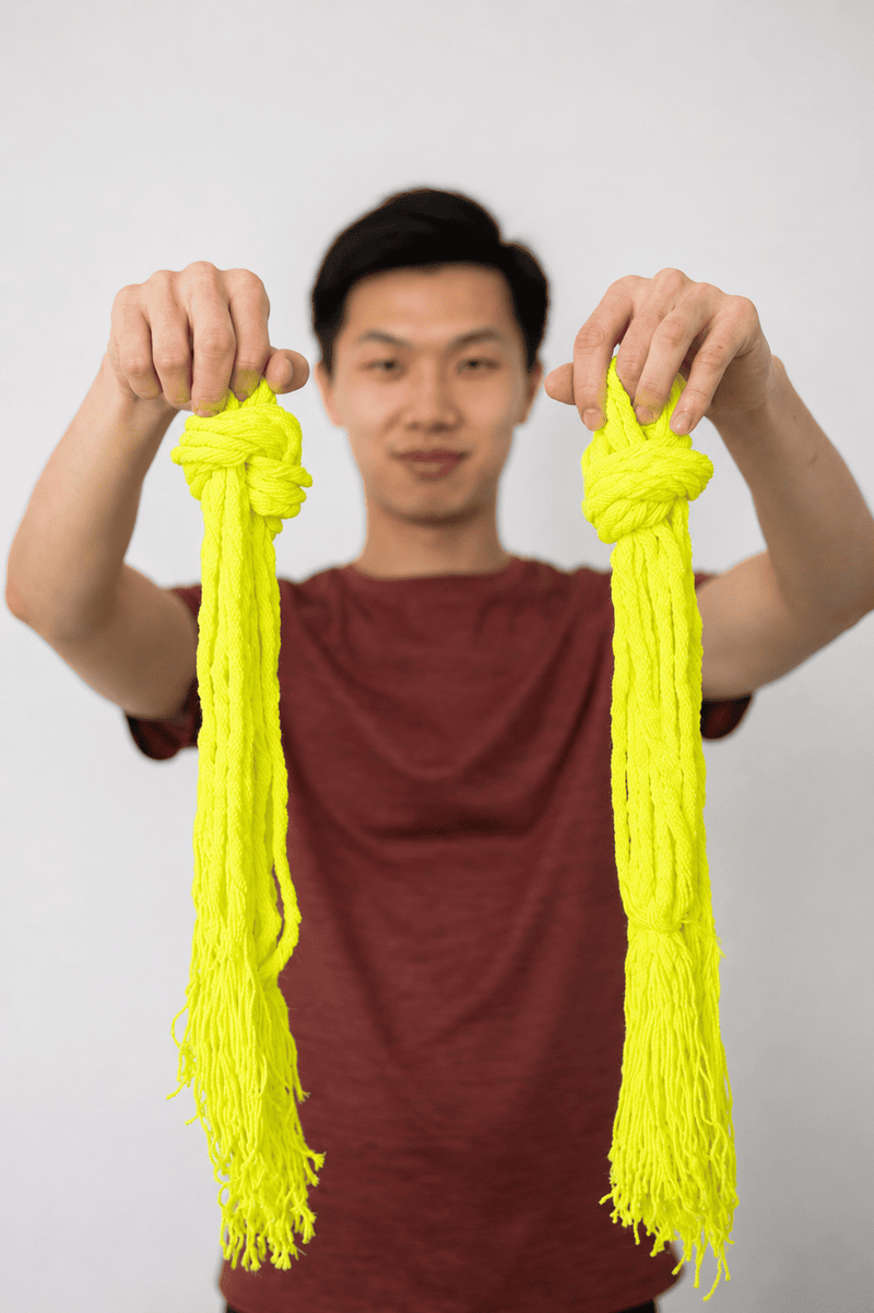Allon Chen holding bundles of neon yellow yo-yo strings in focus against a clean blurred background