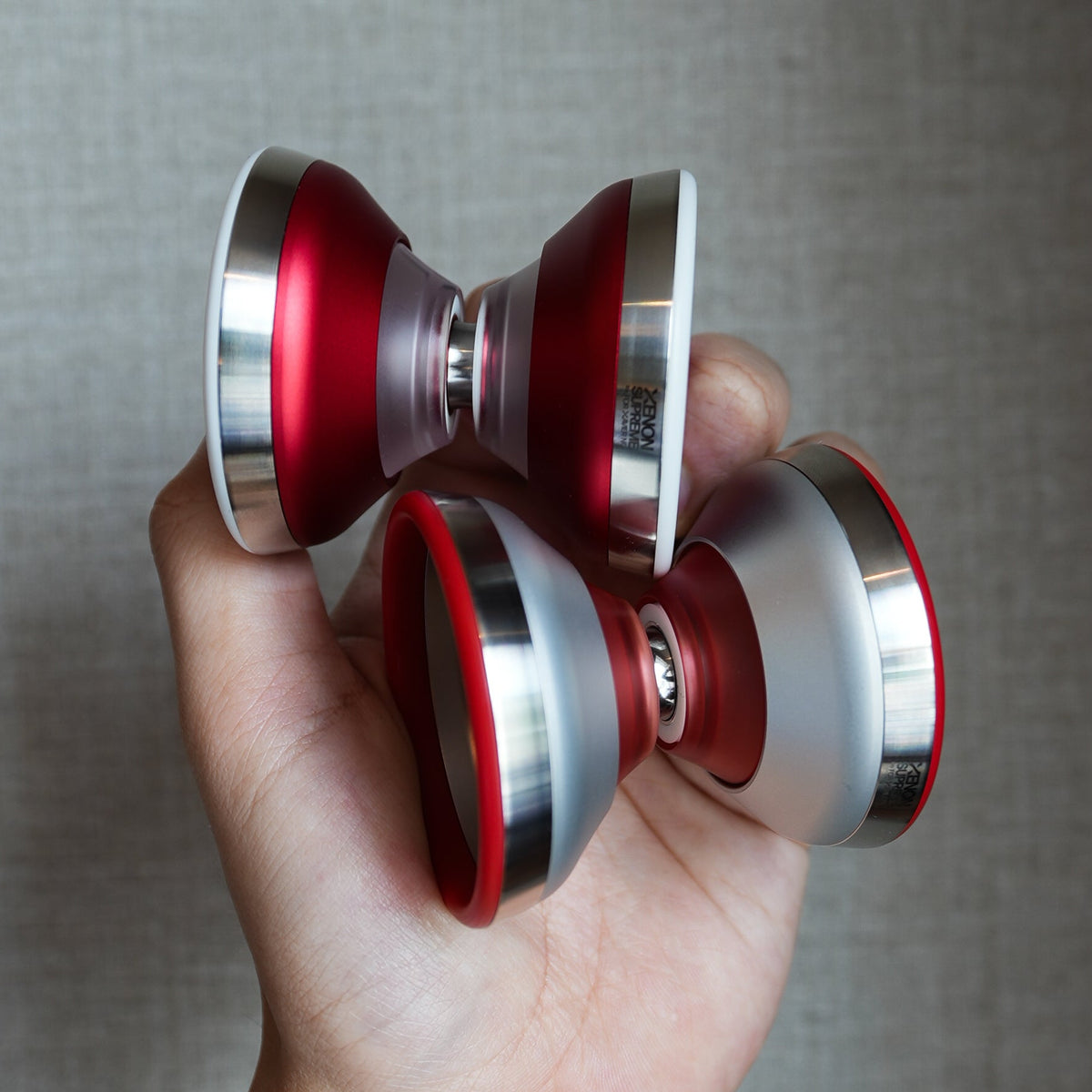 Two XENON SUPREME yoyos in Xavier Red and Blasted Silver held in one hand
